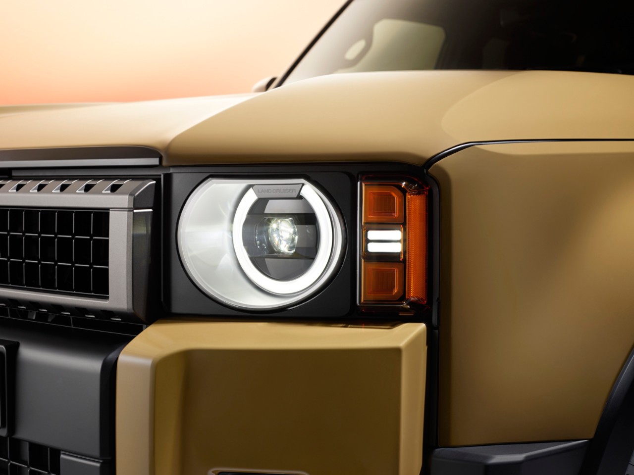 A front view of the all-new Toyota Land Cruiser parked at an angle. Its bright metallic gold paint contrasts with the orange studio setting.